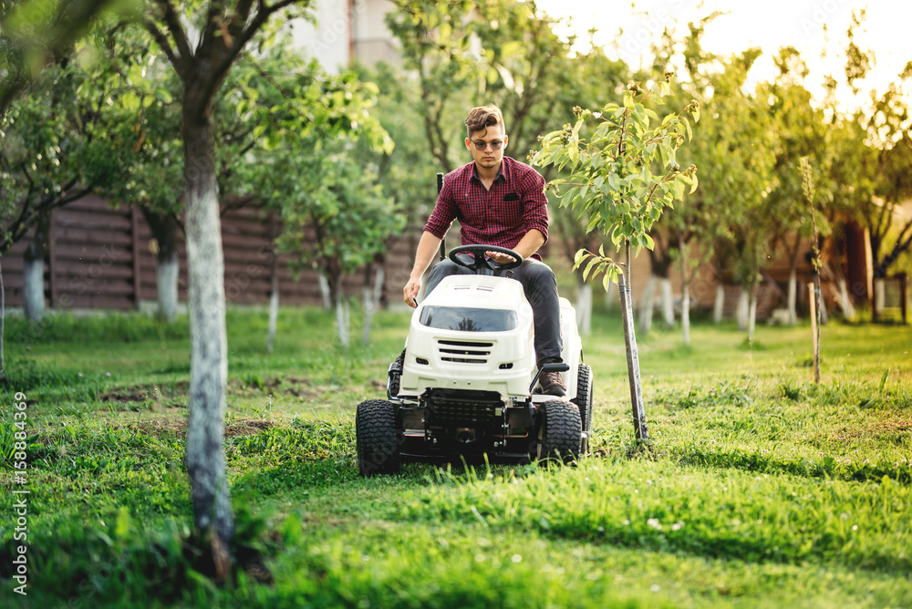 fancy Gardner cutting grass, using professional rideon lawnmower and doing landscaping works