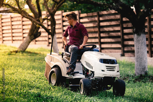 Gardner mowing backyard grass with motorised vehicle. Landscaping details