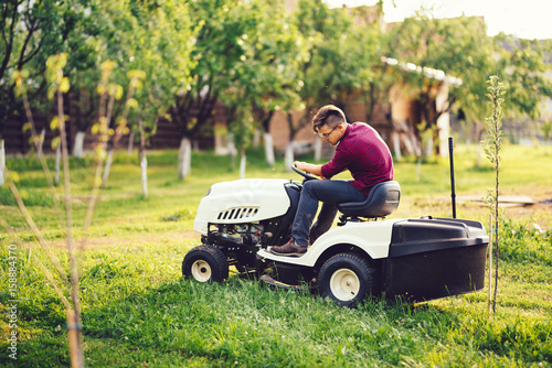 Gardening details, industrial gardner working with ride-on lawnmower and cutting grass in garden