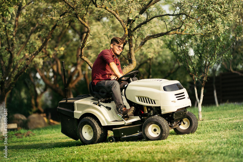 happy handsome worker using ride-on tractor lawn mower