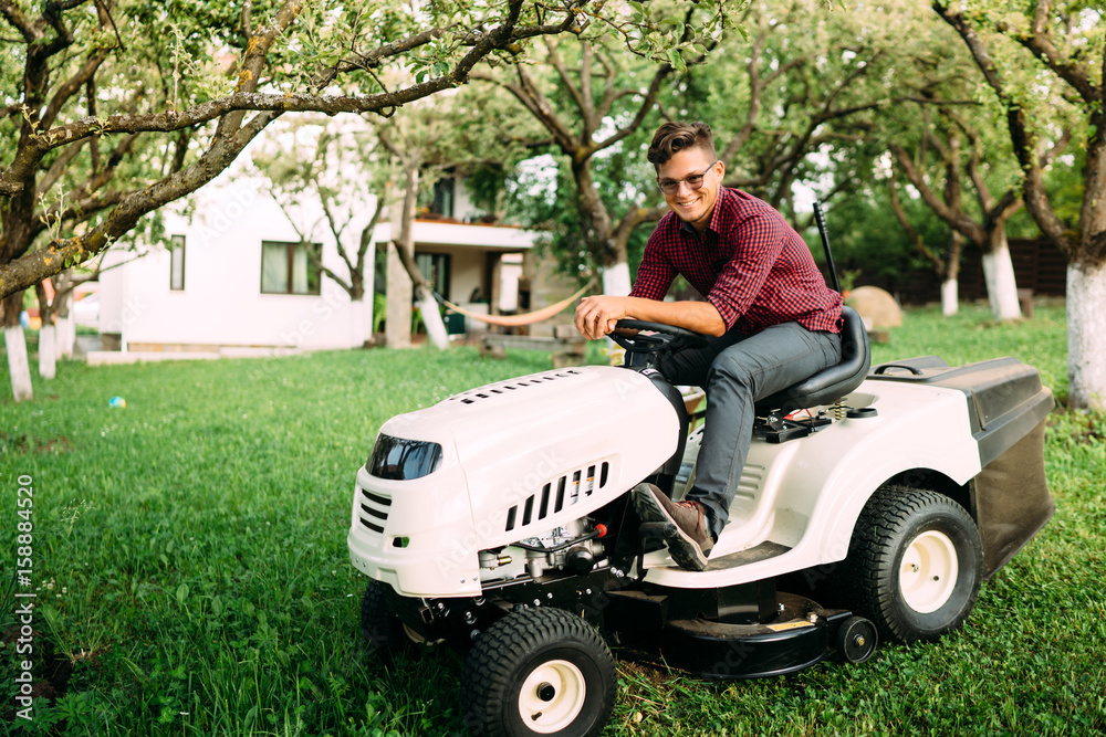 Fototapeta premium Gardening details, grass trimming in progress. Male worker using lawnmower and smiling