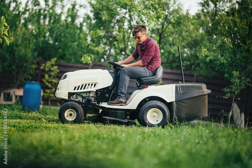 Worker using lawn mower for cutting grass in garden