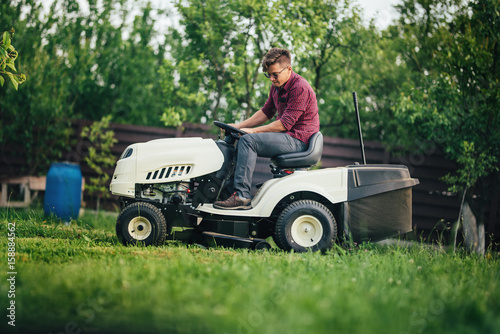 Worker using lawn mower for cutting grass in garden