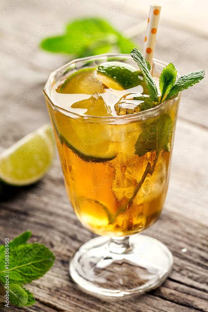 Tasty fresh refreshing summer tea drink with ice, cold tea, lime and mint in glass on wooden background. Closeup. Tasty fresh refreshing summer tea drink with ice, cold tea, lime and mint in glass on wooden background. Closeup.