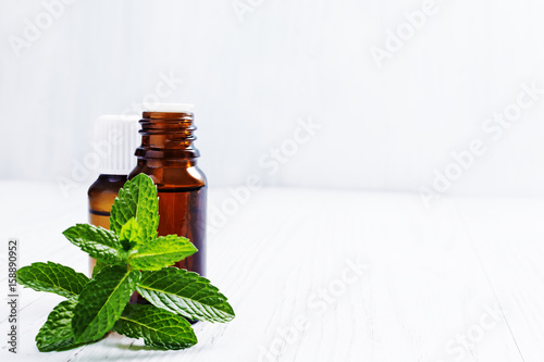 Essential oil of peppermint in dark bottles, fresh green mint on white wooden background, selective focus