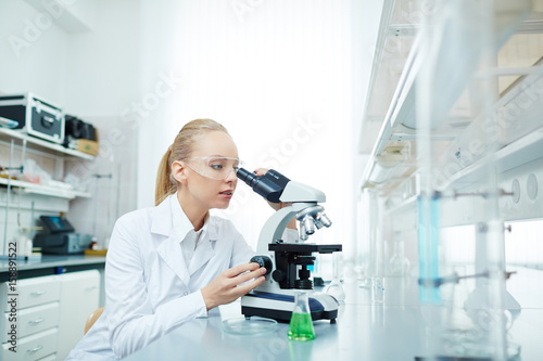 Portrait of beautiful blond scientist using microscope working on medical research in modern laboratory