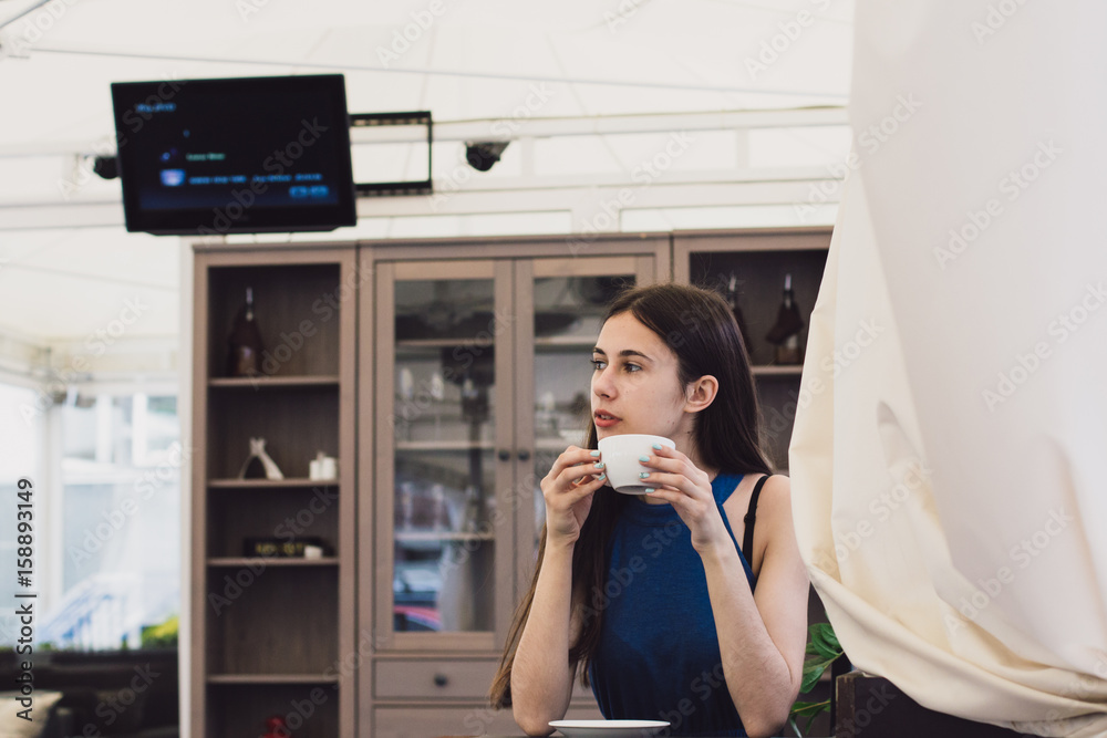 A very beautiful business woman sits in a cafe and holds a cup of coffee in her hands A very beautiful business woman sits in a cafe and holds a cup of coffee in her hands