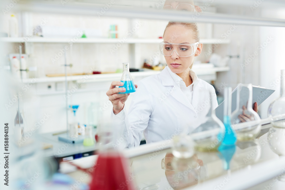 Portrait of beautiful female chemist working on research in modern laboratory holding test tubes with colored liquid Portrait of beautiful female chemist working on research in modern laboratory holding test tubes with colored liquid