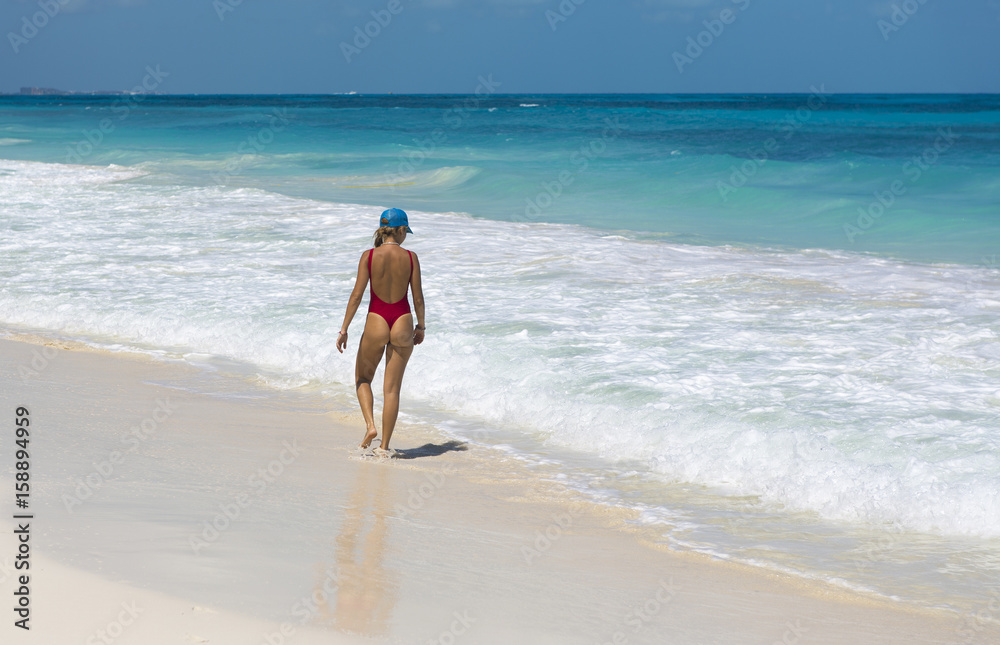 Sexy and tanned lady walking on the beach. Turquoise water. Vacation concept image.