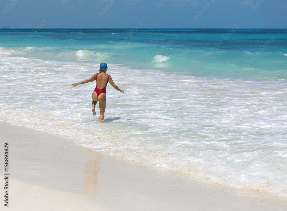 Sexy lady walking on the beach and splashing water happily. Turquoise water. Vacation concept image.