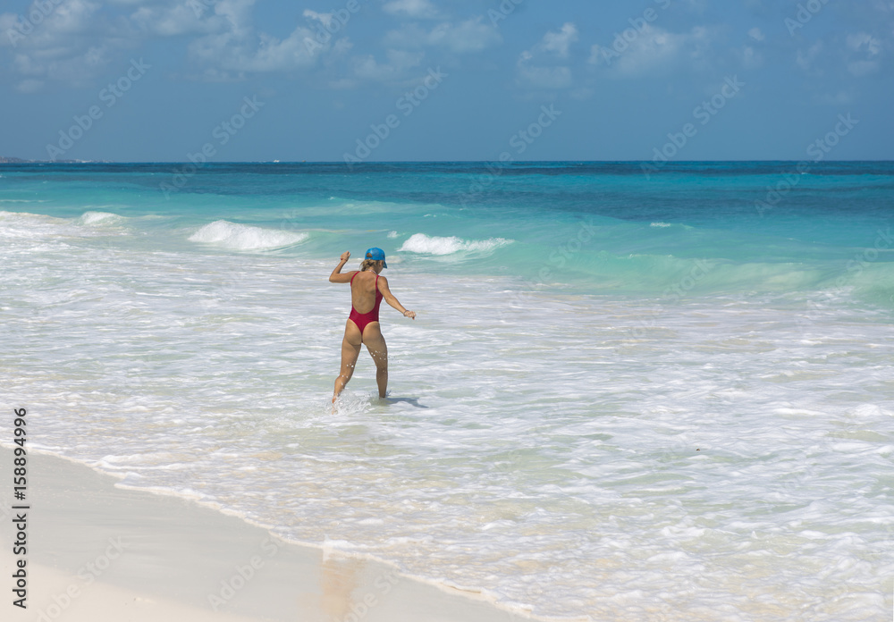 Sexy lady walking on the beach and splashing water happily. Turquoise water. Vacation concept image.