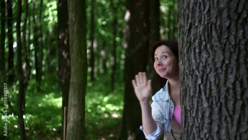 young woman silly funny waving from behind a tree in the forest young woman silly funny waving from behind a tree in the forest