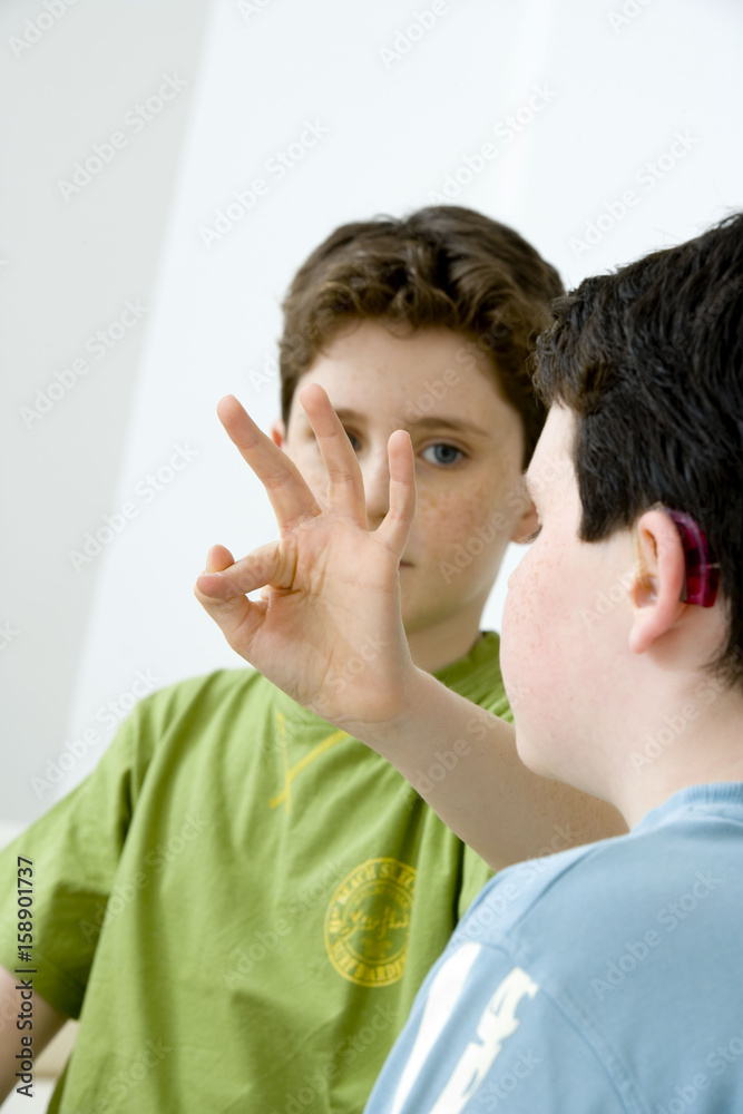 Fototapeta premium Models Do not use for HIV Young boy using the French sign language to discuss with his hearing-impaired brother The French sign language uses signs to designate words but also dactylology (each letter of the alphabet is represented by a defined position of the fingers then enabling to spell a word) and the lip reading The young boy designates the letter \f\ (see image nᄚ0833202 ans series of images from nᄚ0572308 to 0574108 to see the other letters of the alphabet)