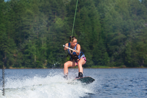 slim brunette woman riding wakeboard on lake