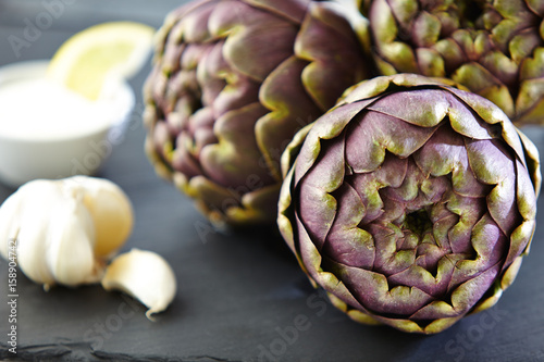 three artichokes with garlick bulb, dip and lemon slice