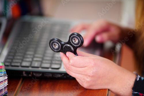 Young woman holding a popular fidget spinner toy in her hand while she is working in her computer on office background photo