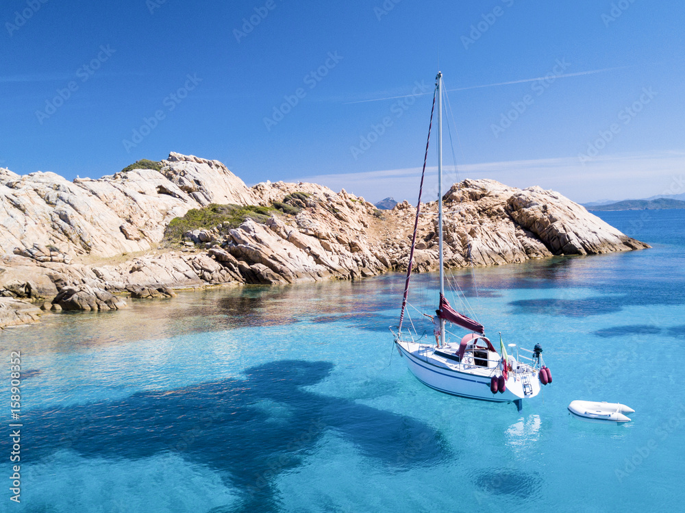 Aerial view of a sail boat in front of Mortorio island in Sardinia. Amazing beach with a turquoise and transparent sea. Emerald Coast, Sardinia, Italy...