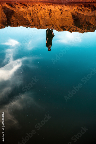 Reflection in the water of a girl standing on a sandy beach