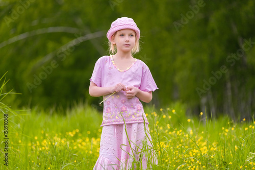 Adorable blonde girl in  pink hat and clothes posing on sunset on meadow with flowers