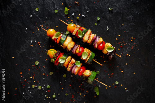 Vegetarian skewers with halloumi cheese and mixed vegetables on black background, top view