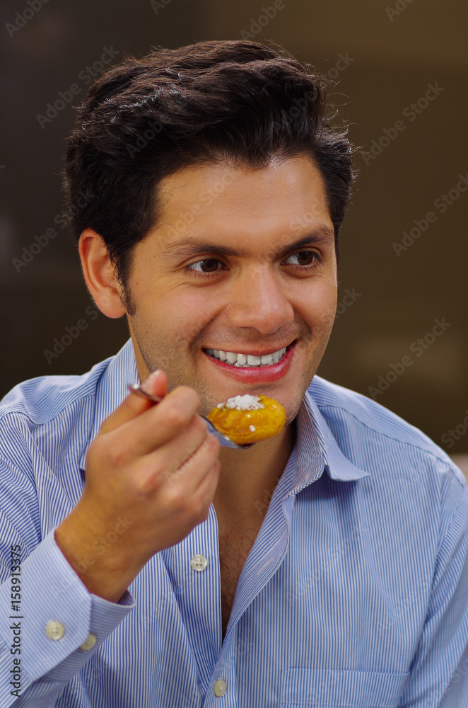 Handsome man eating a delicious turkish dessert sekerpare with coconut powder in a brown background Handsome man eating a delicious turkish dessert sekerpare with coconut powder in a brown background