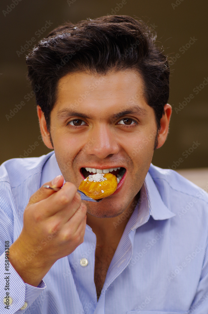 Handsome man eating a delicious turkish dessert sekerpare with coconut powder in a brown background Handsome man eating a delicious turkish dessert sekerpare with coconut powder in a brown background