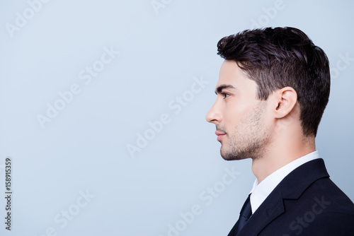 Side profile photo of a young handsome brunete realtor with bristle in a formal wear, standing on the pure blue background next to copyspace photo