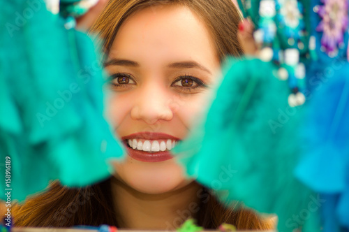Close up of a smiling woman hiding behind a magenta catchdreamer, in colorful market background