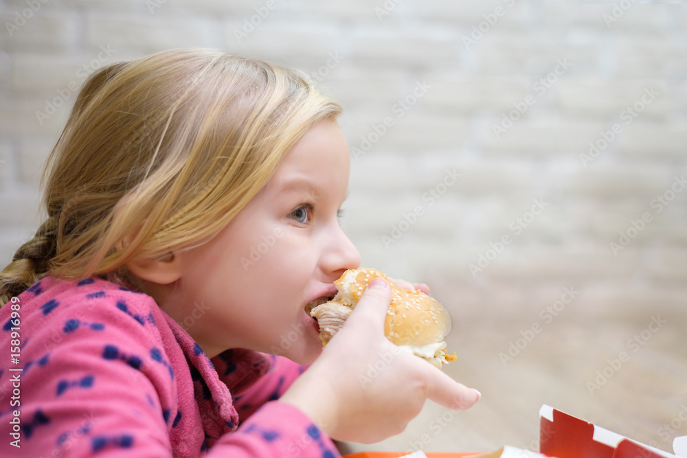 Adorable girl eat classic burger in fast food restaurant