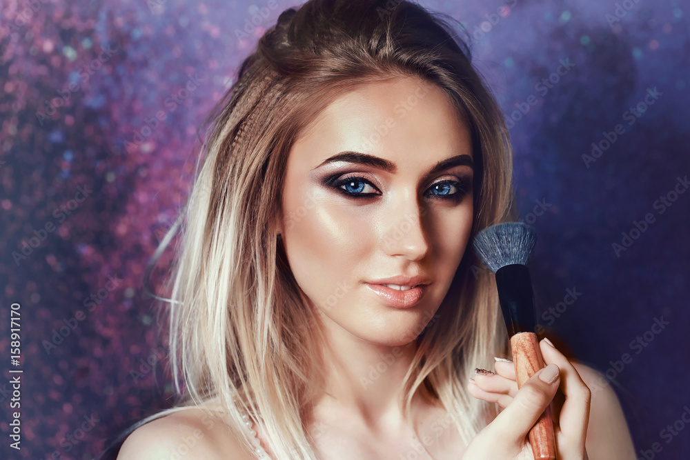 Beautiful young girl with blue eyes posing with tassel for applying makeup. Portrait of a model