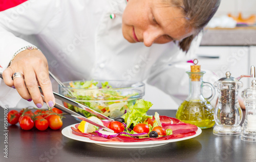rofessional cook prepares a plate with salami and fresh salad