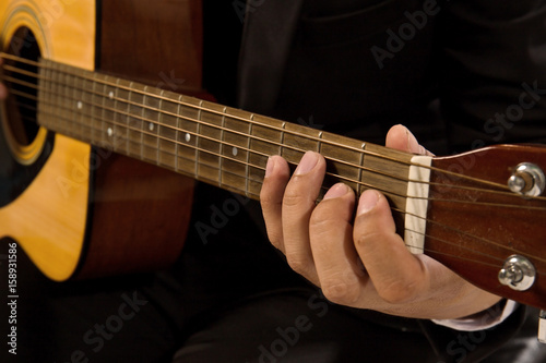 Close-up a young man in a black suit playing guitar isolated on black backgroud.