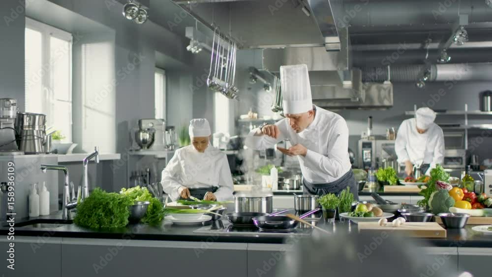 Famous Chef Works in a Big Restaurant Kitchen with His Help. Kitchen is Full of Food, Vegetables and Boiling Dishes. Shot on RED EPIC-W 8K Helium Cinema Camera.