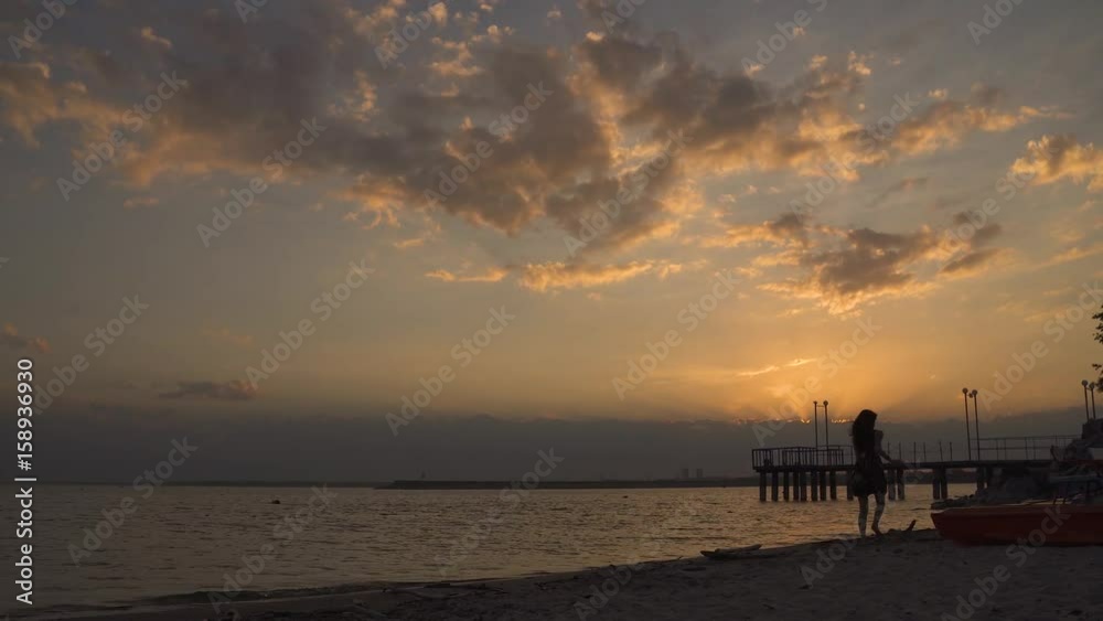 Silhouette of a girl in a light dress on the beach at sunset. Beautiful young girl running along the sand barefoot. Silhouette of a girl in a light dress on the beach at sunset. Beautiful young girl running along the sand barefoot.