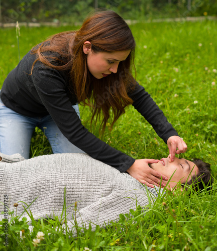 Beautiful woman giving fisrt aid to a handsome young man, cardiopulmonary resuscitation, in a grass background photo