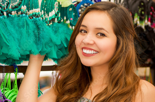 Close up of a beautiful smiling young woman touching a colorful catchdreamers, in colorful market fabrics background
