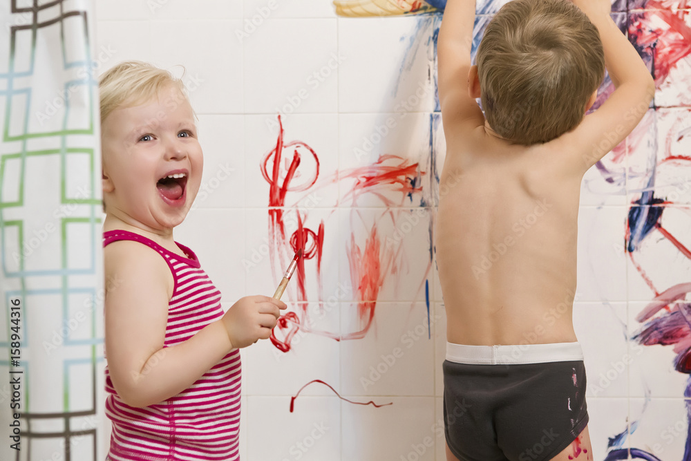 Naklejka premium Portrait of two cute adorable white Caucasian little boy and girl playing painting on walls in bathroom, having fun, lifestyle active childhood concept, early education development