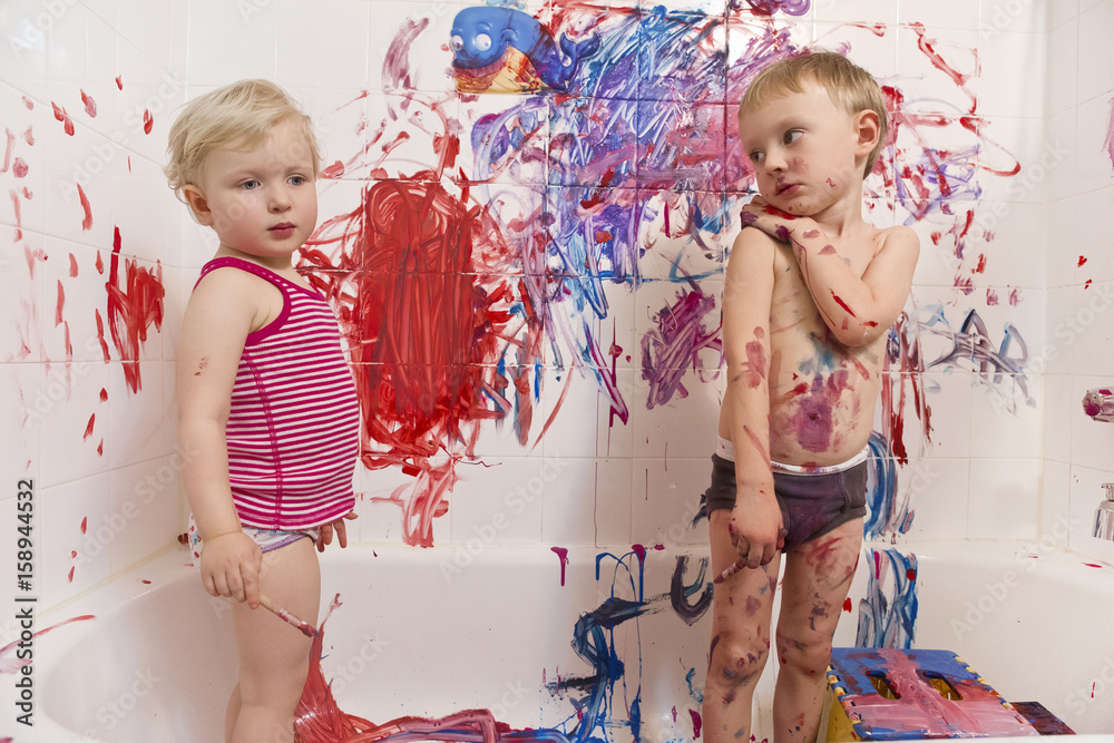 Fototapeta premium Portrait of two cute adorable white Caucasian little boy and girl playing painting on walls in bathroom, having fun, lifestyle active childhood concept, early education development