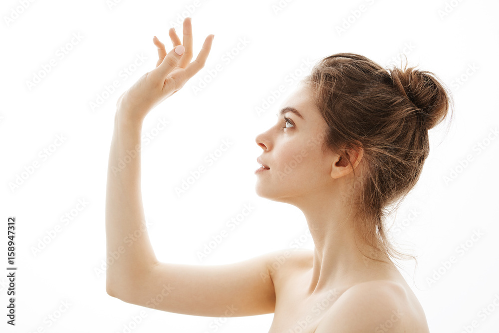 Obraz premium Portrait of young beautiful tender naked girl with bun posing in profile over white background.