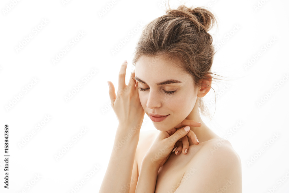 Young tender nude girl with bun posing over white background. Closed eyes. Young tender nude girl with bun posing over white background. Closed eyes.