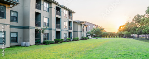 View from grassy backyard of a typical apartment complex building in suburban area at Humble, Texas, US. Sunset with warm light. Panorama style.