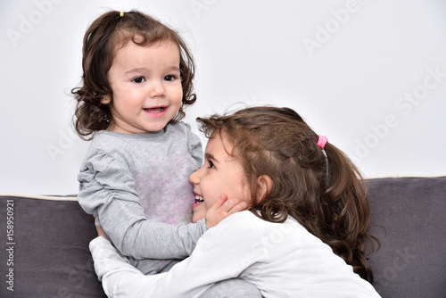 Hugging and smiling sisters playing on the sofa