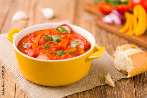 Delicious letcho with fresh vegetables, served in a yellow pot with the fresh bun. photo