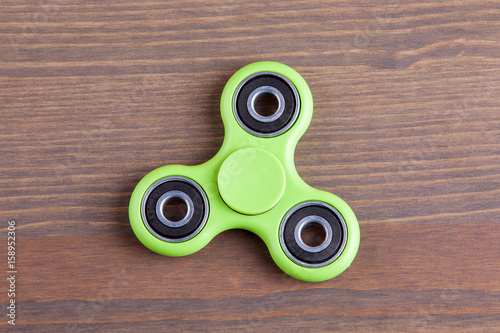 Green fidget spinner stress relieving toy on wood background.