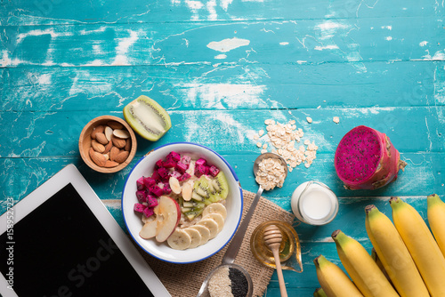 Bowl of oatmeal porridge with bananas, apple, dragon fruit and almonds. Top view photo