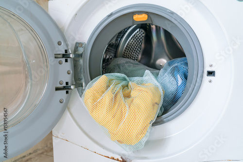 Colorful shirt and trousers in a white laundry. A close up of a washing machine loaded with clothes