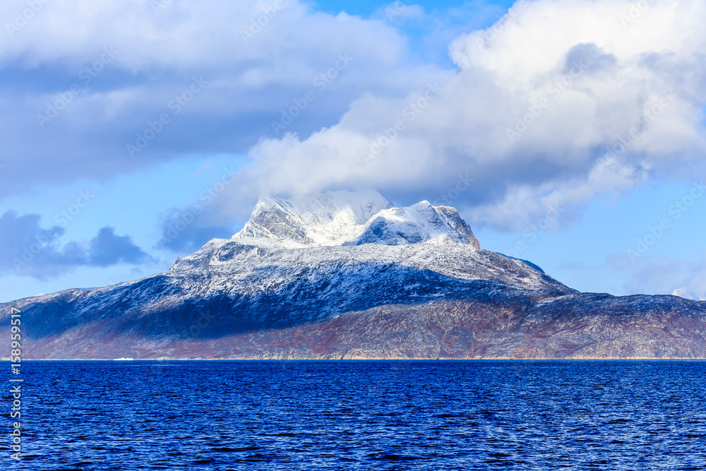 Clouds over Sermitsiaq mountain covered in snow with blue sea in the foreground, nearby Nuuk city, Greenland Clouds over Sermitsiaq mountain covered in snow with blue sea in the foreground, nearby Nuuk city, Greenland