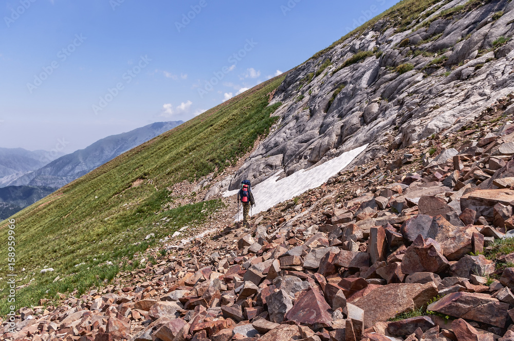 Альпинист с рюкзаком идет по склону в горах, солнечная погода