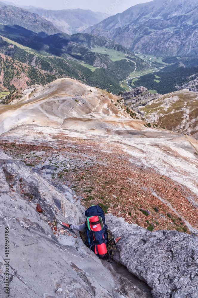 Альпинист с рюкзаком спускается по каменному уступу на фоне горного пейзажа