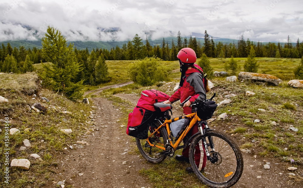 The photo was taken during a cycling trip through the Altai in the summer in August. Russia. Cyclist woman, girl standing and looking at the mountains, closeup. The photo was taken during a cycling trip through the Altai in the summer in August. Russia. Cyclist woman, girl standing and looking at the mountains, closeup.
